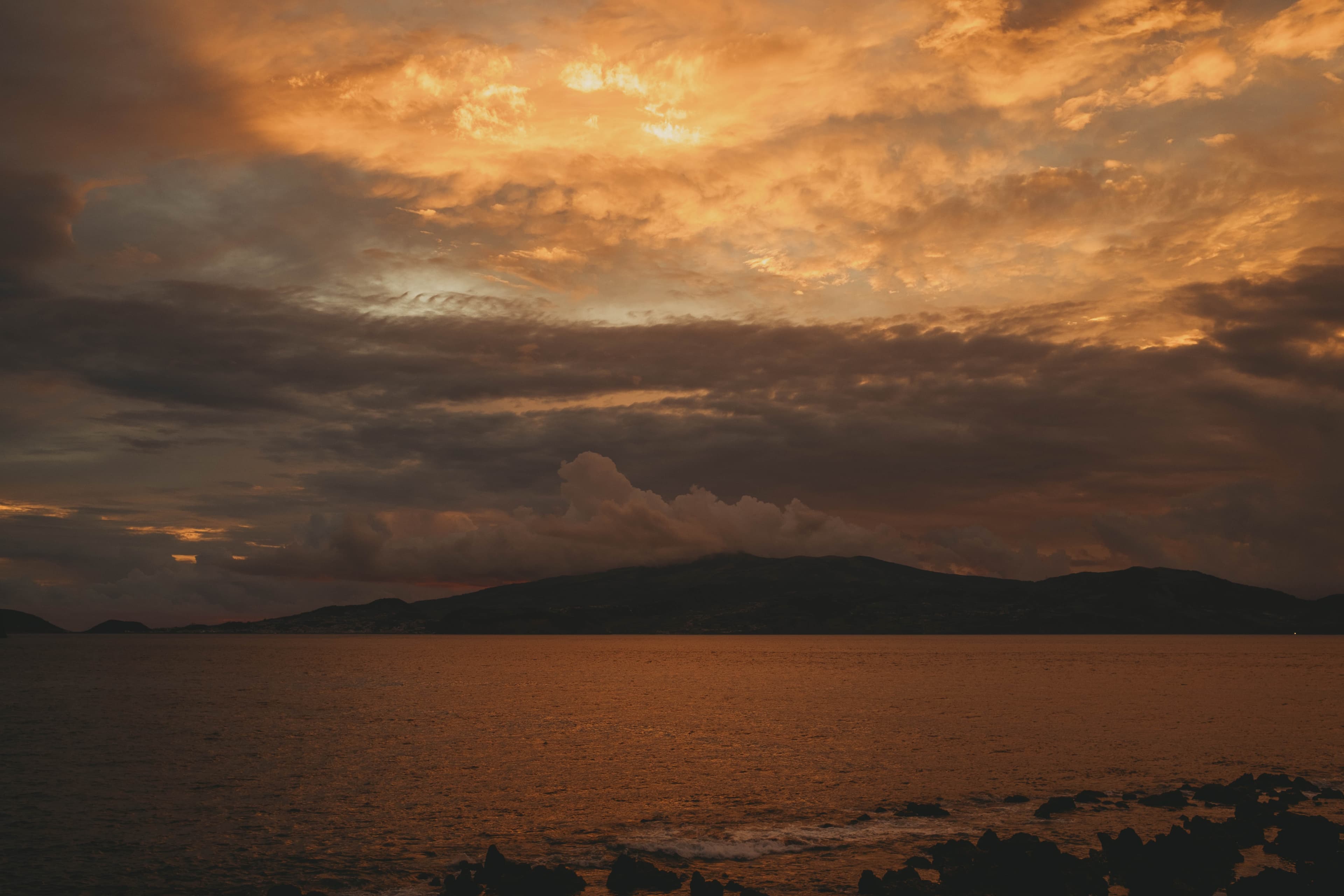 Dramatic golden sunset sky over the Atlantic Ocean viewed from Cella Bar with neighboring islands silhouetted on the horizon and volcanic rocks in the foreground reflecting the warm light