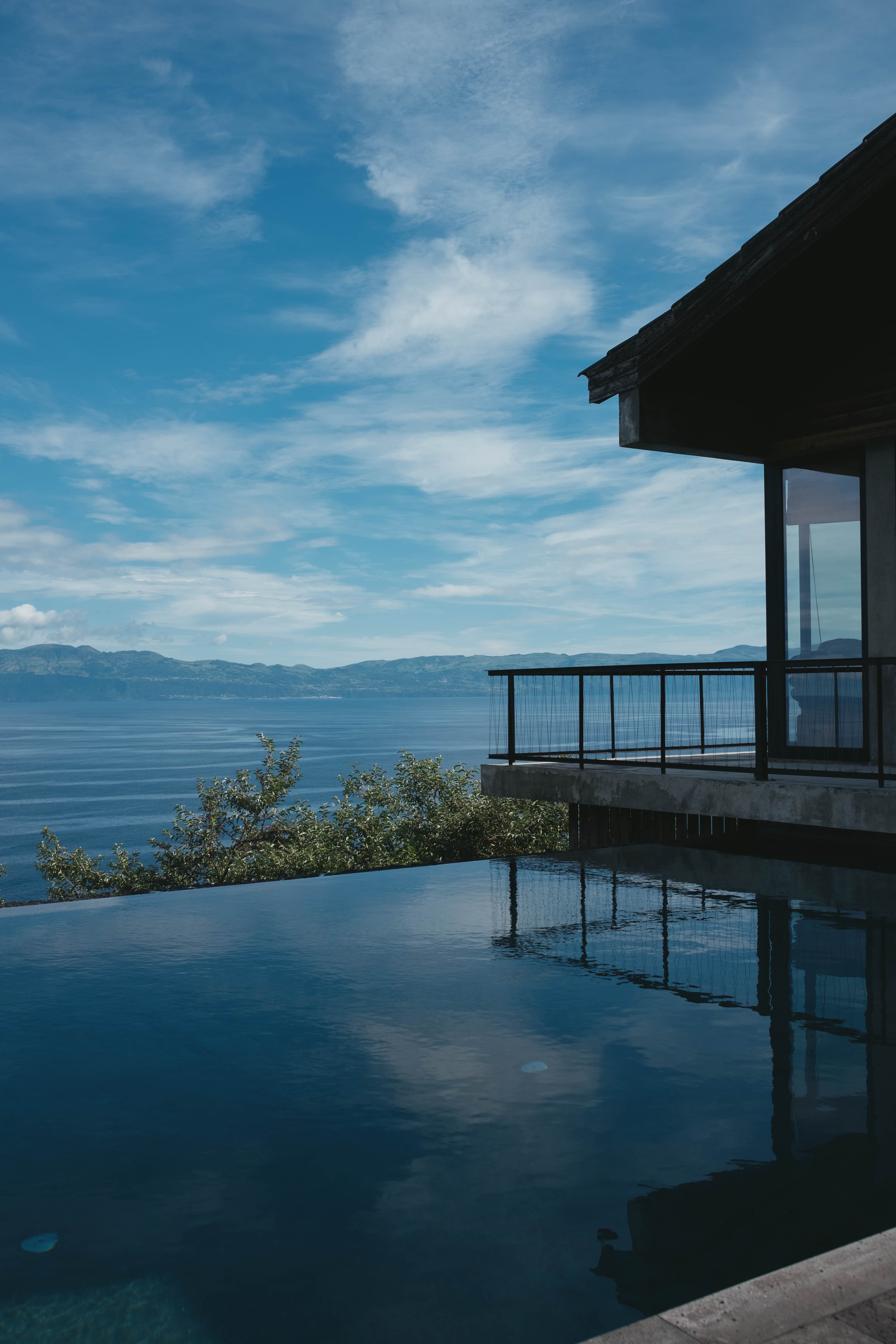 Modern house with steel balcony and infinity pool overlooking the Atlantic Ocean, with distant island of São Jorge under a partly cloudy sky