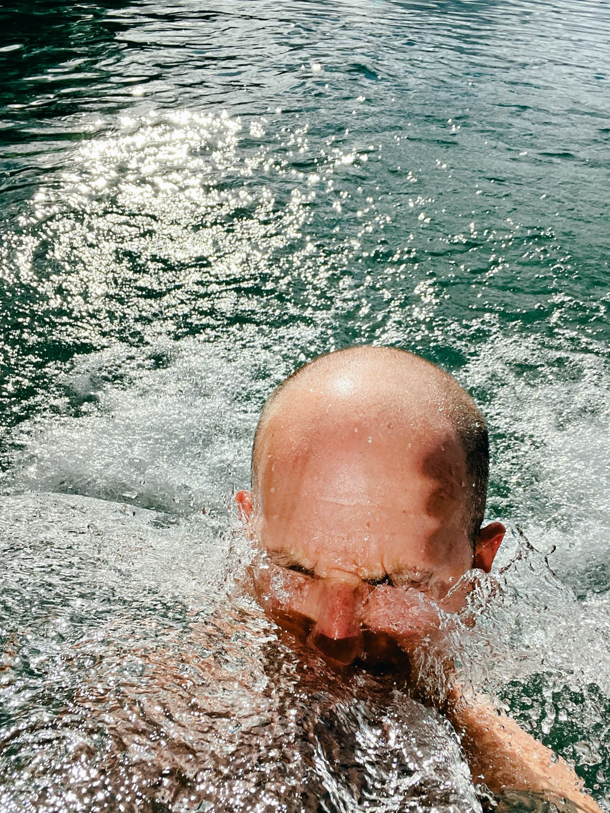 Selfie of me emerging from churning turquoise water with eyes closed, surrounded by white foam and splashing waves