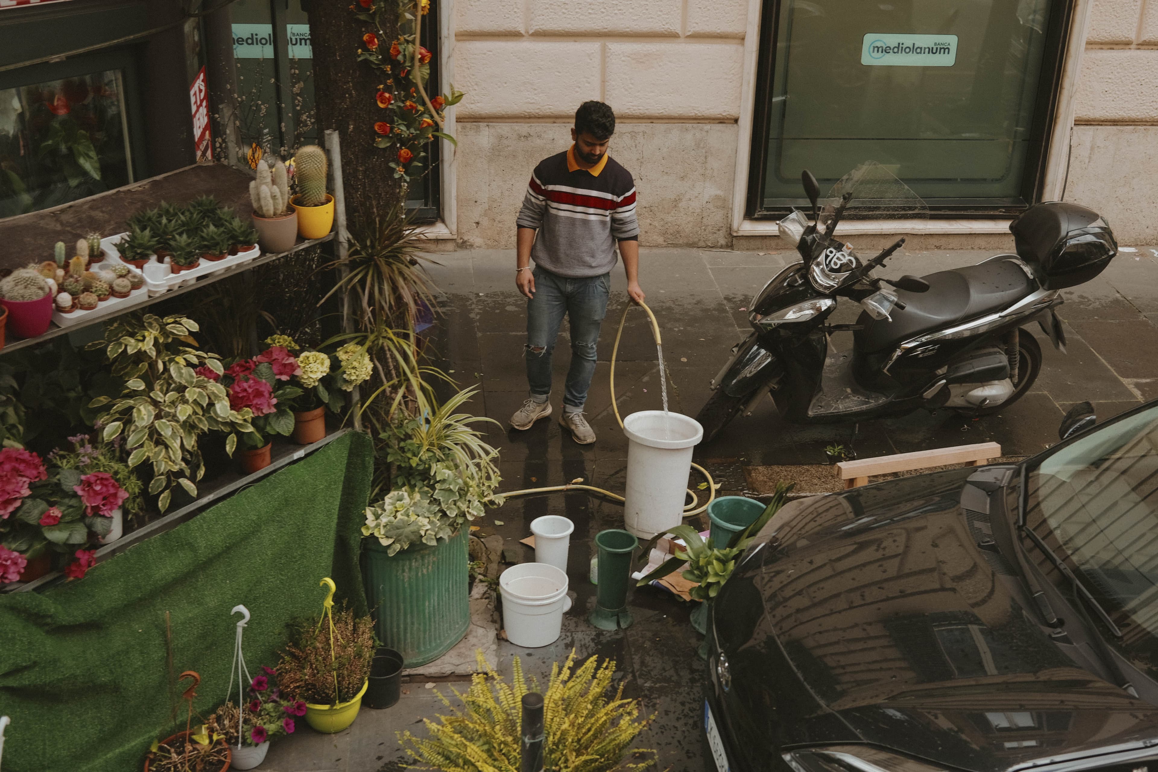 A man, working at a flower stand, filling a bucket of water with a hose